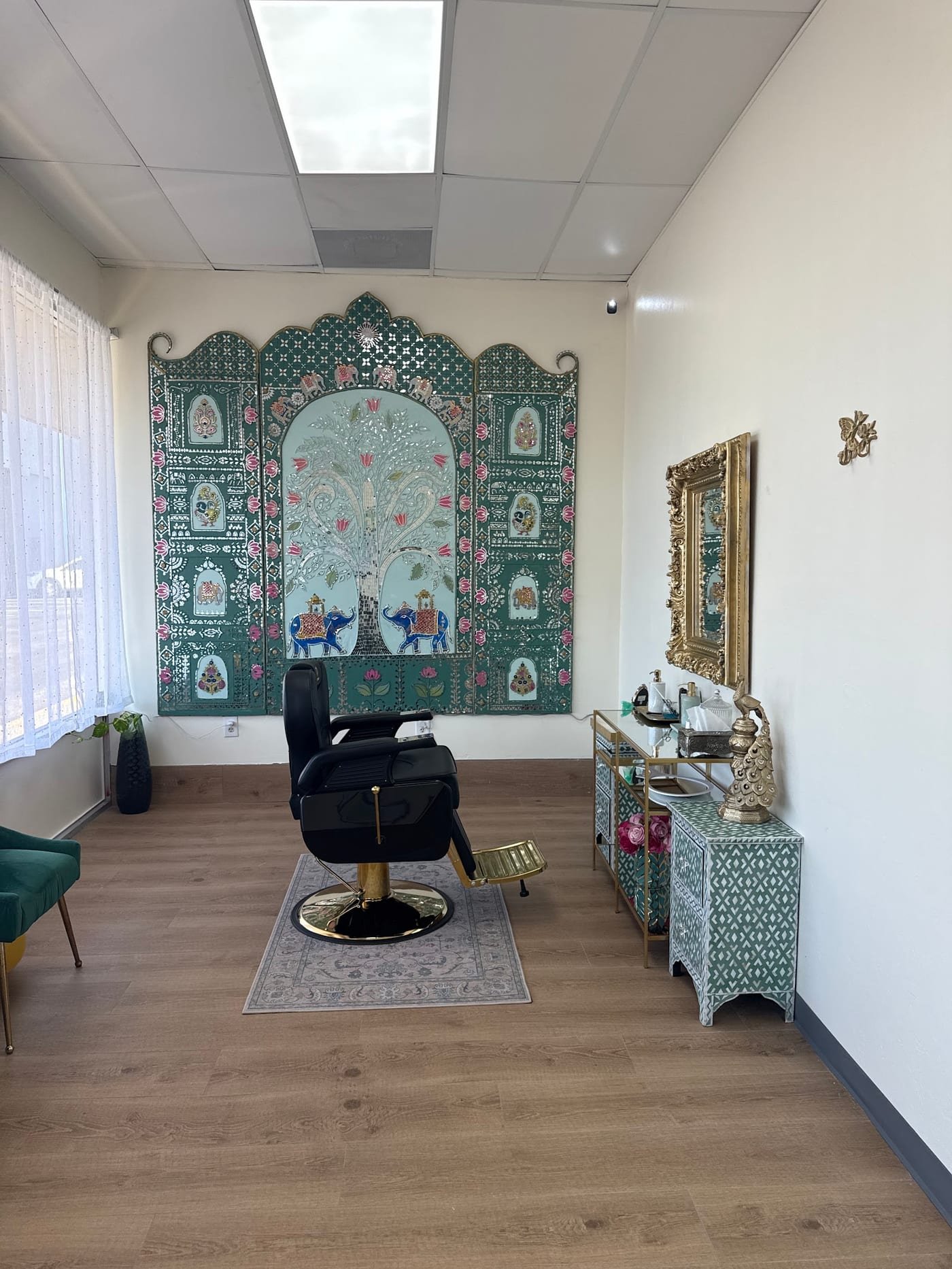 A hand-painted Jaipur mirror-work panel of a tree, elephants and peacocks behind a gold styling chair at I Salon Spot